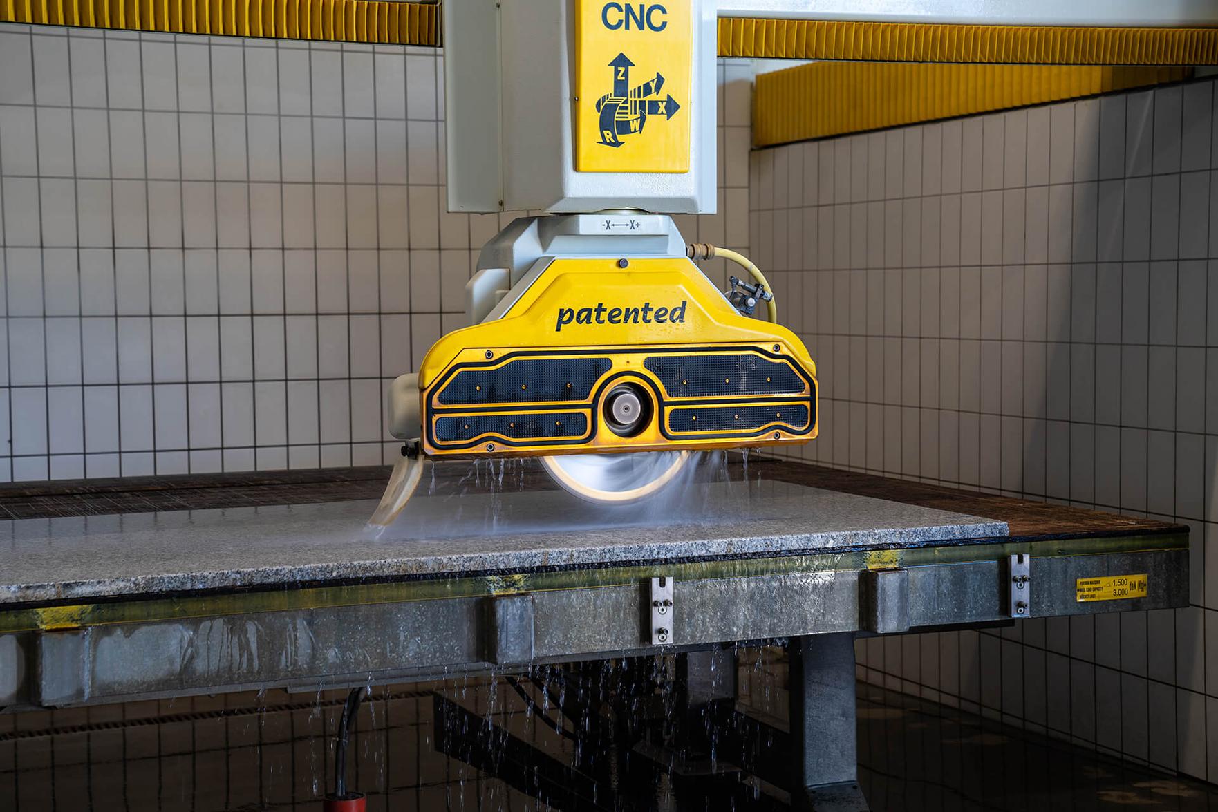 CNC-Brückensäge schneidet eine Granitplatte unter Wasserkühlung im Pung Steinwerk Bonn